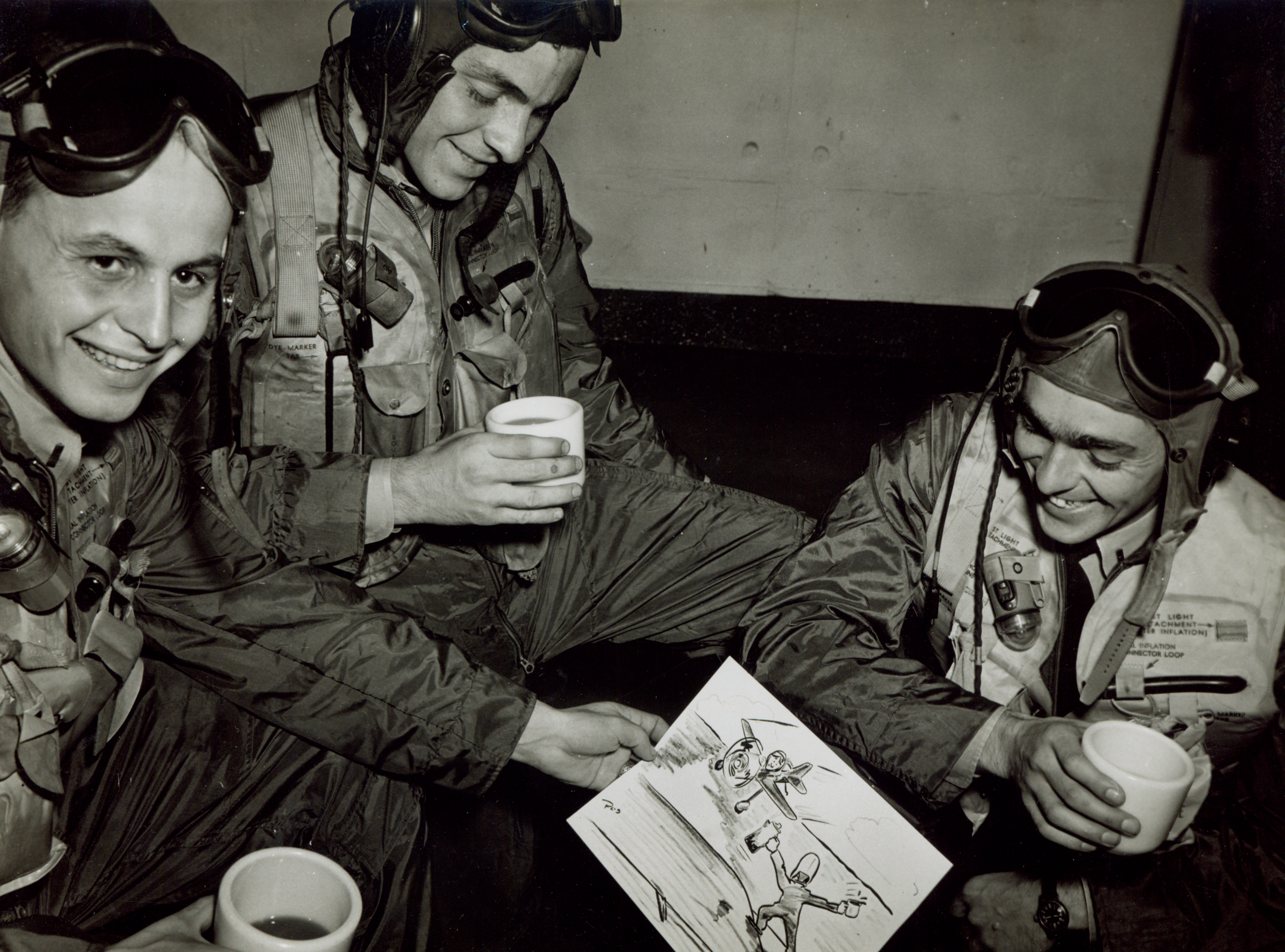 Three crew members sharing coffee while examining a sketch of fellow crew members on the flight deck.