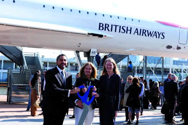 Three people standing in front of a British Airways aircraft, holding oversized scissors and a cut ribbon.