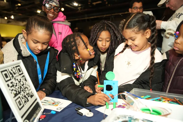 A group of children is engaged in a hands-on educational activity, examining and working on a small robot model together.