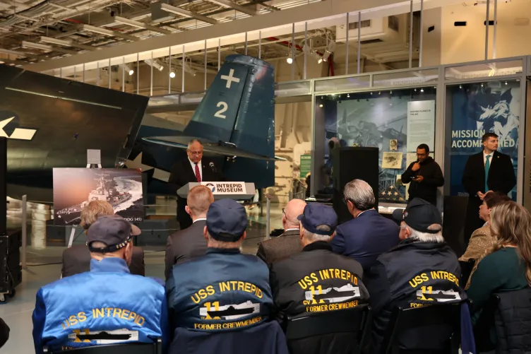 Mr. Del Toro stands at the podium on the hangar deck of the Intrepid Museum.