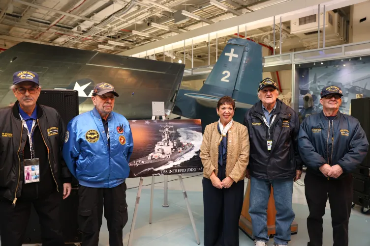 Mrs. Betty Del Toro and four formal crew members stand together on the hangar deck of the Intrepid Museum.