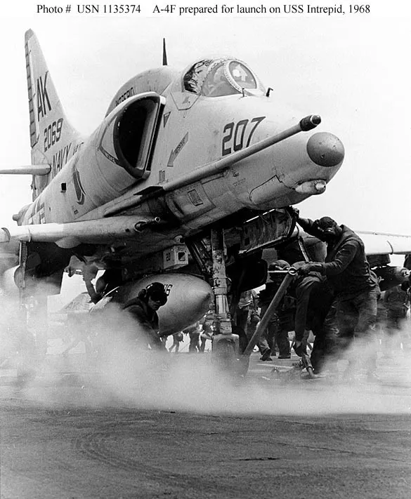 An archival photo of an airplane on the flight deck with men and smoke around it.