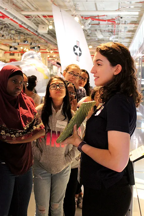 A Museum educator is showing something on a tablet to a group of students.