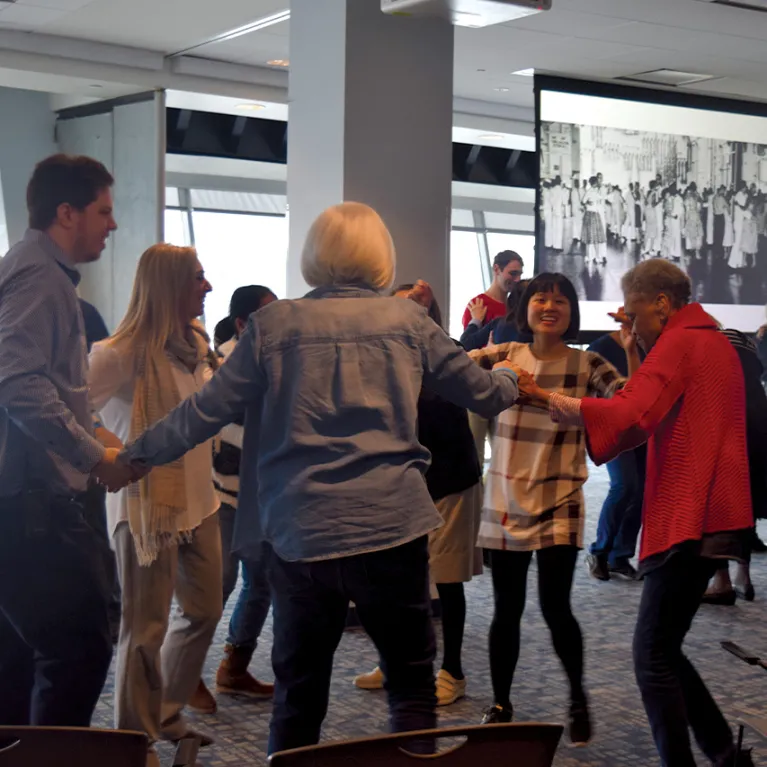 Visitors are standing in a circle and holding hands dancing.