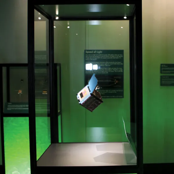 A holographic cube is suspended in mid-air in a display case.