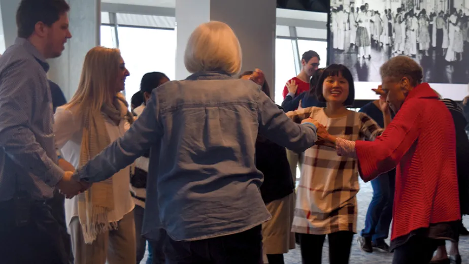 Visitors are standing in a circle and holding hands dancing.