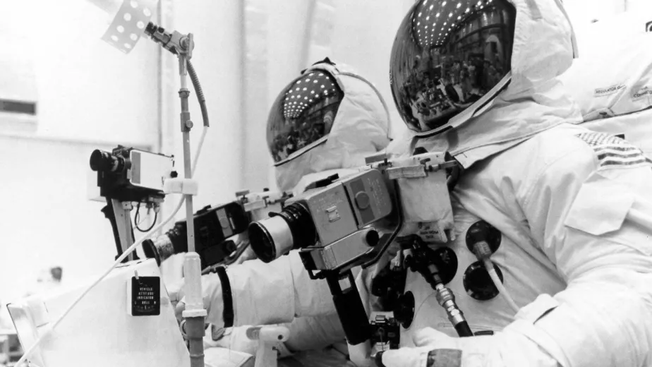 Astronauts in space suits peering through a camera.